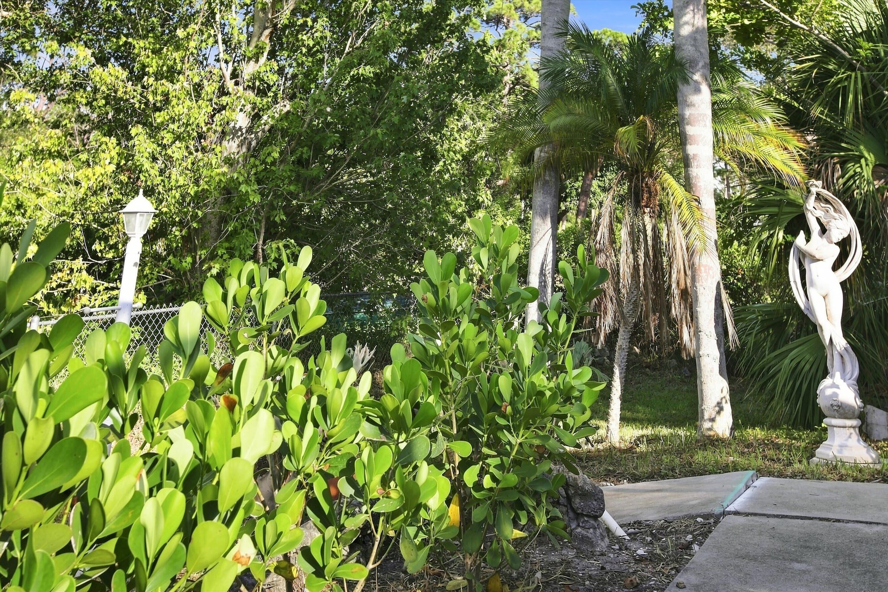 A garden with various plants, a white statue, and a lamp post.