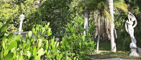 A garden with various plants, a white statue, and a lamp post.