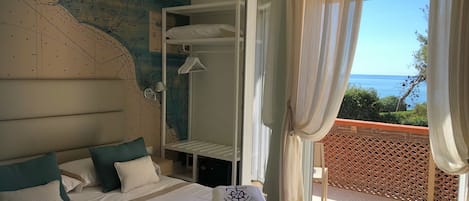 A hotel room with a large map on the wall, a bed with a white comforter, and a view of the sea through a balcony.