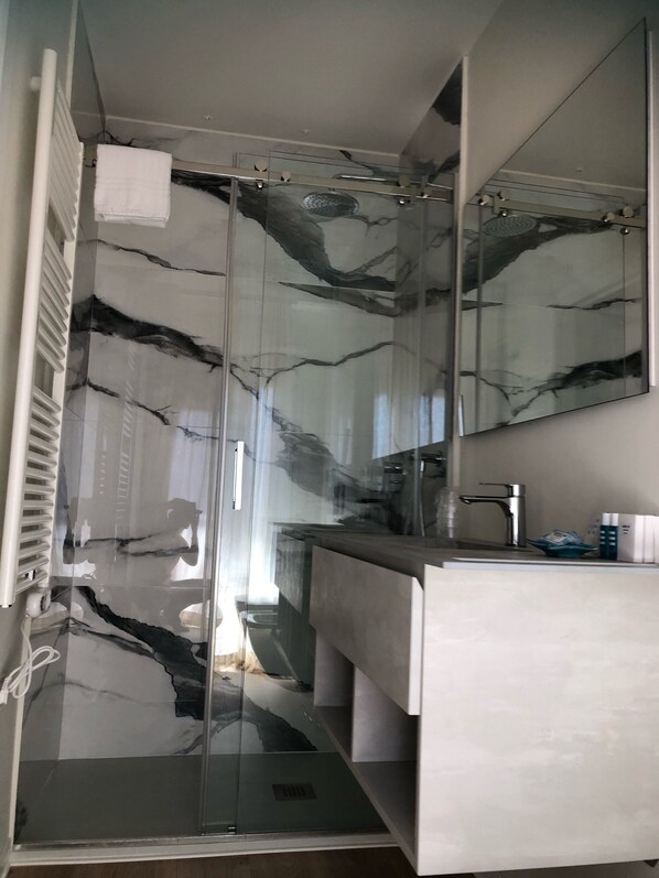 A modern bathroom with a glass shower enclosure, a white sink, and a large mirror.