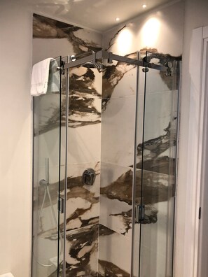 Una cabina doccia in vetro con decorazione murale in marmo.