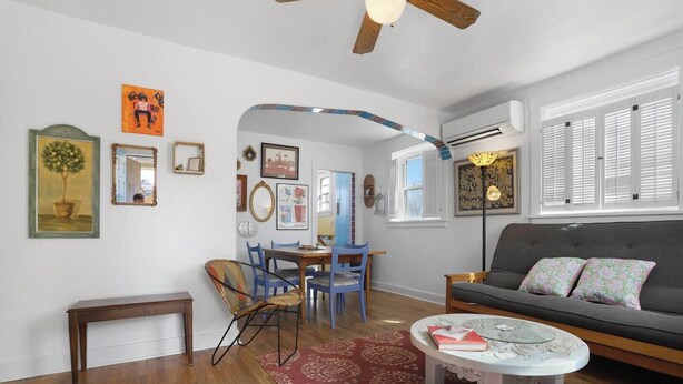 Un salon comprenant un canapé, une table basse et des fauteuils, un coin repas avec une table et des chaises, et un couloir agrémenté d’un miroir et d’œuvres d’art.