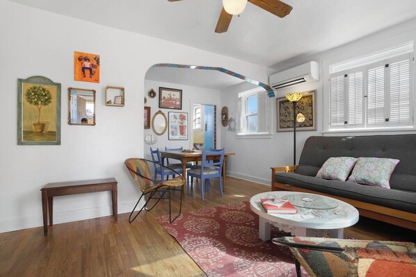 A living room with a sofa, coffee table, and chairs, a dining area with a table and chairs, and a hallway with a mirror and artwork.