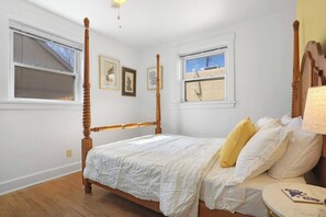 Una camera da letto con un letto a baldacchino, due finestre e un comodino con una lampada.