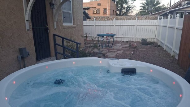 Jacuzzi al pati d'una casa amb mur de pedra, tanca de fusta i taula.