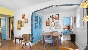 Un coin repas avec une table et des chaises en bois, un buffet bleu aux portes vitrées et un tapis rouge à motifs.