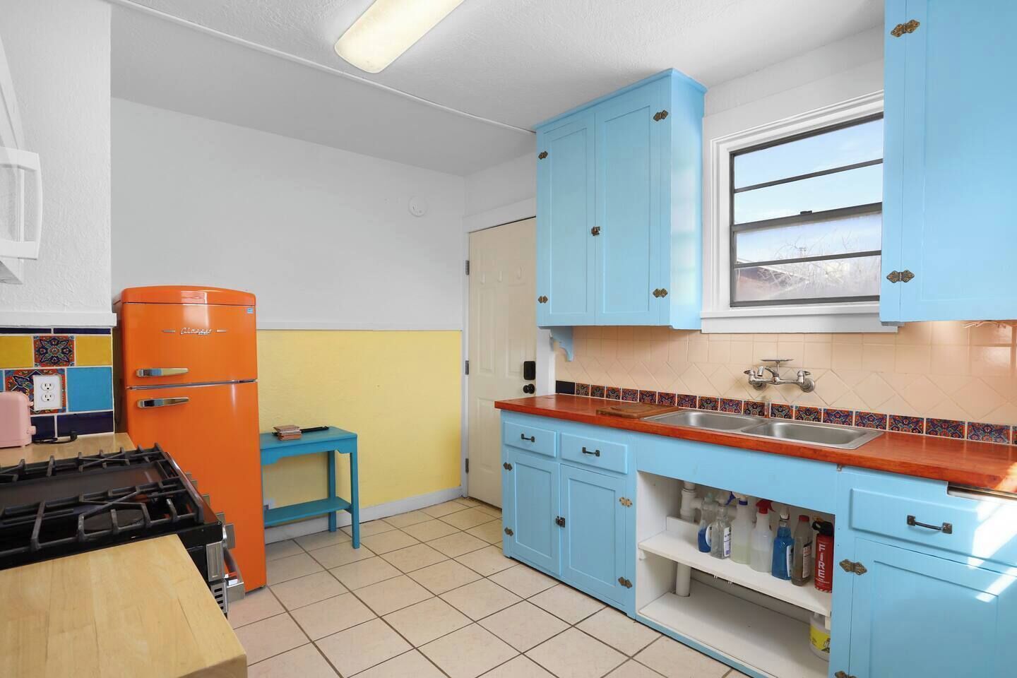 A kitchen with blue cabinets, a red refrigerator, and a tiled backsplash.