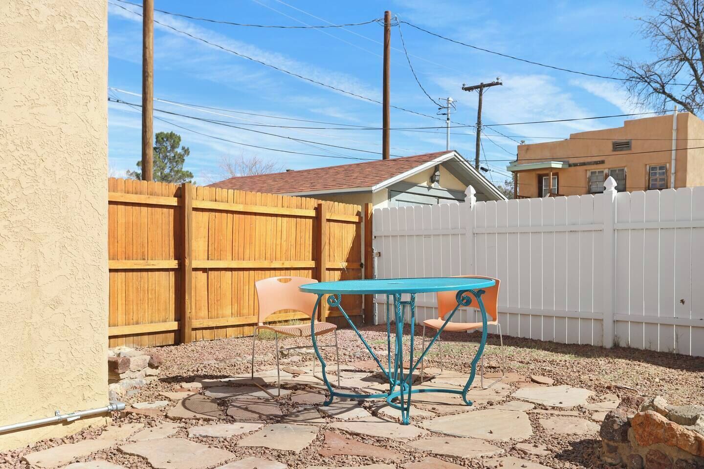 A backyard with a wooden fence, a turquoise metal table, and a white picket fence.