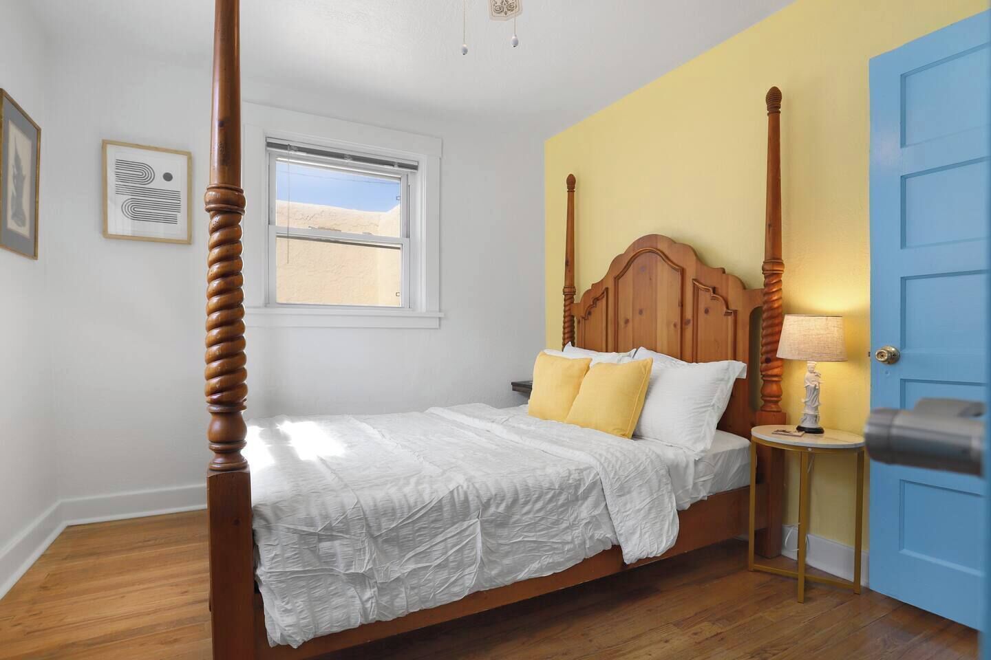A four-poster bed with a wooden headboard, a bedside table with a lamp, and a window with a view of the desert.