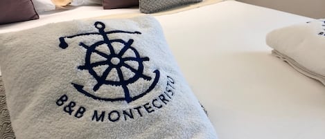 A neatly made bed with a white blanket featuring a logo and text, accompanied by pillows in various shades.