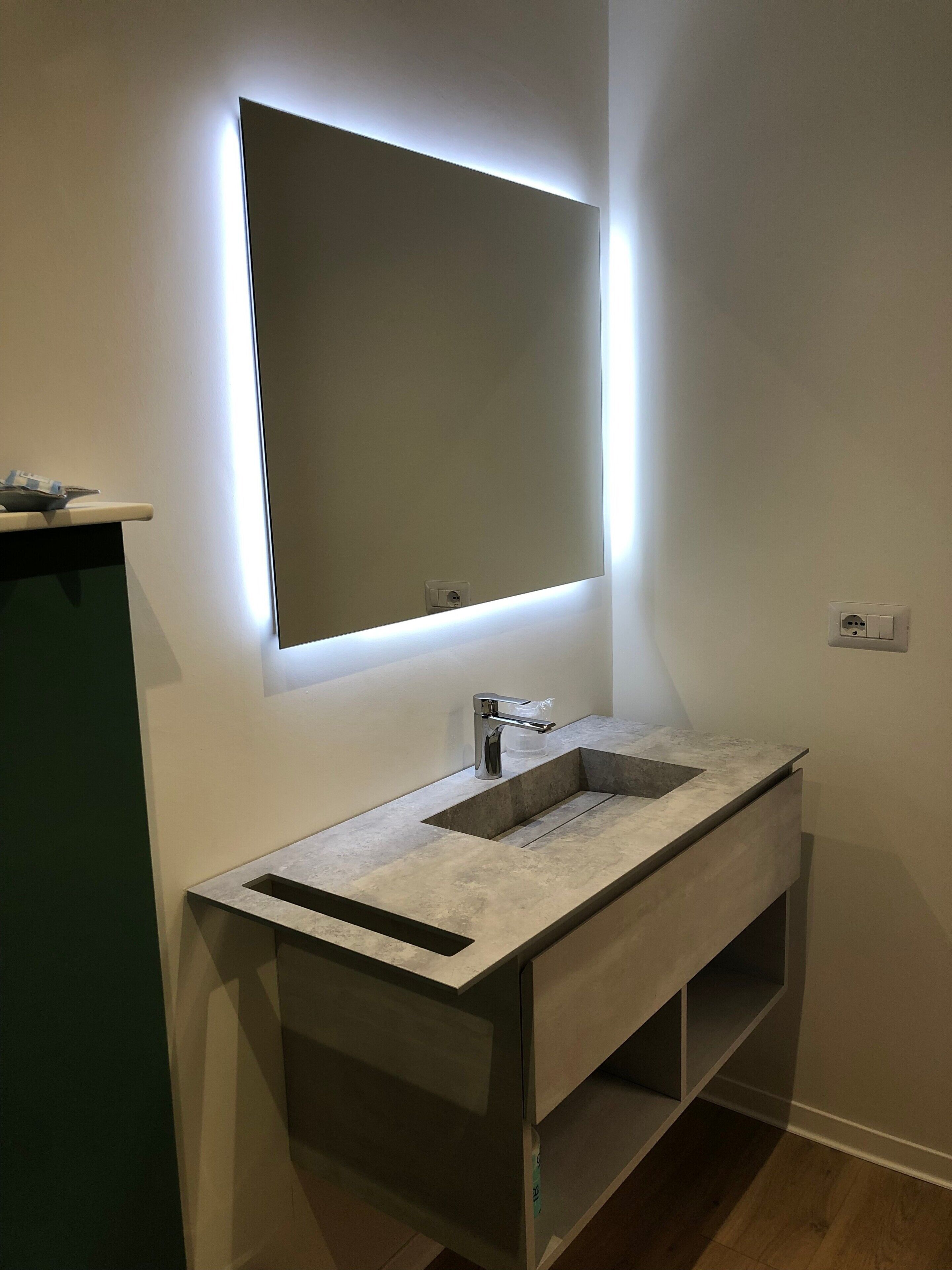 Ein modernes Badezimmer mit integriertem Waschbecken, einem Spiegel und einer Leuchte darüber.