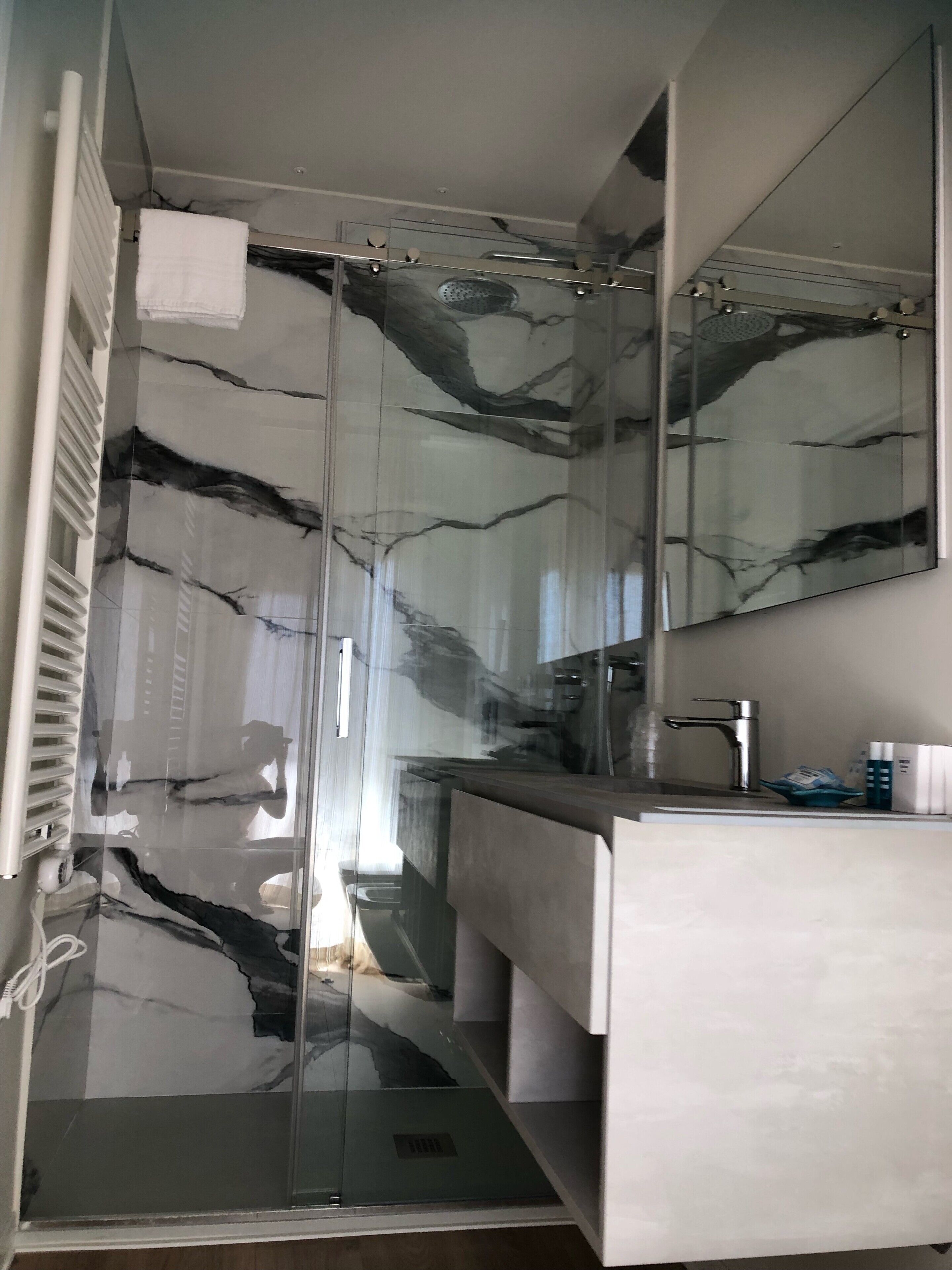 Ein modernes Badezimmer mit Duschkabine aus Glas, einem weißen Waschbecken und einem großen Spiegel.