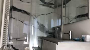 Ein modernes Badezimmer mit Duschkabine aus Glas, einem weißen Waschbecken und einem großen Spiegel.