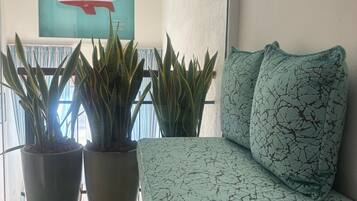 A room with a sofa, two potted plants, a wall-mounted sailboat painting, and a window with curtains.