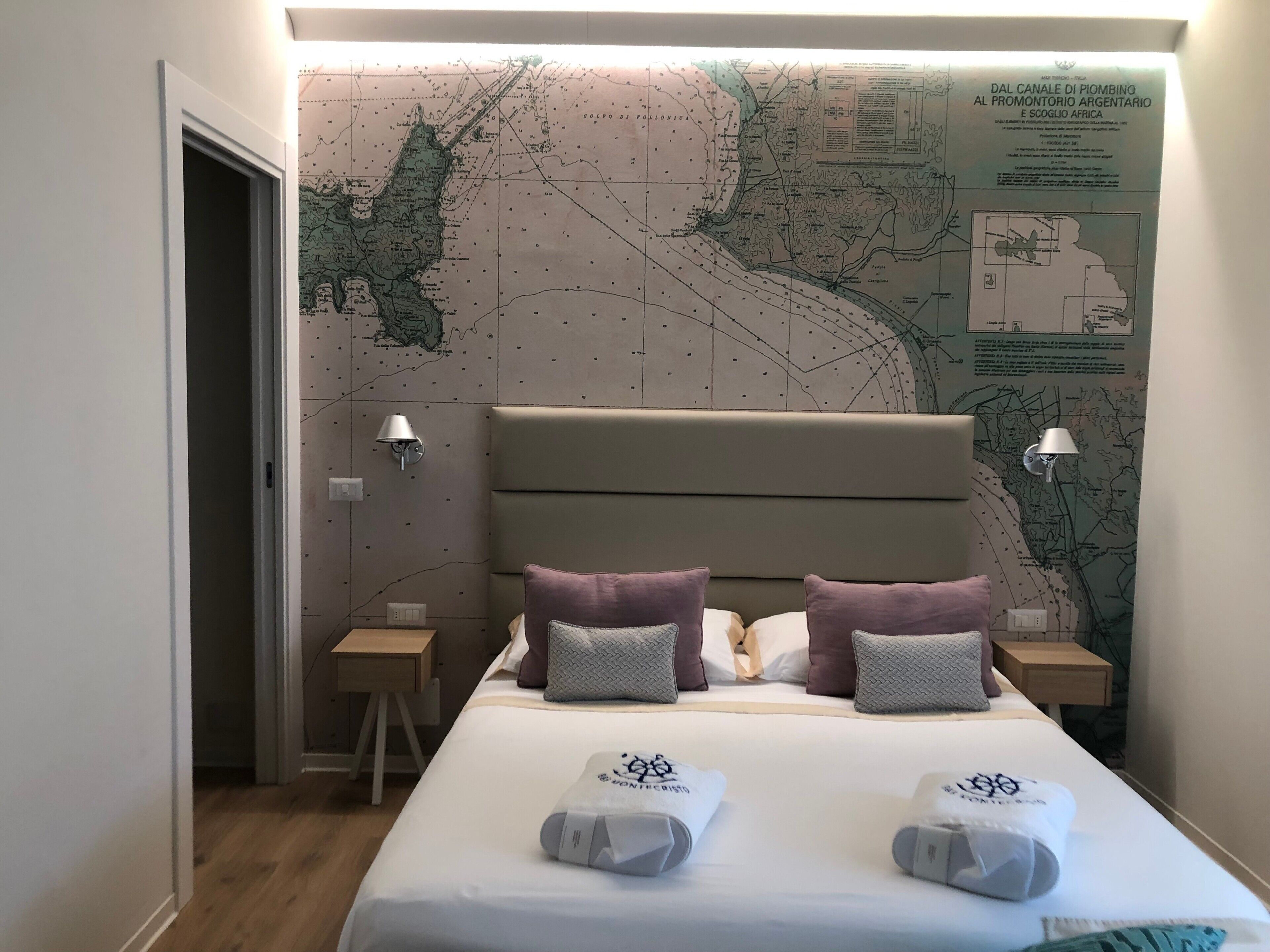 A hotel room with a large map on the wall, a bed with pillows, a nightstand, and a lamp.