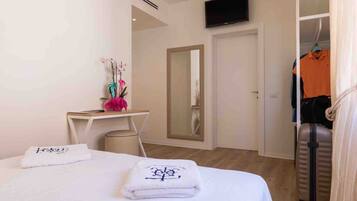 A hotel room with a bed, a desk, a mirror, a TV, and a closet with hanging clothes.