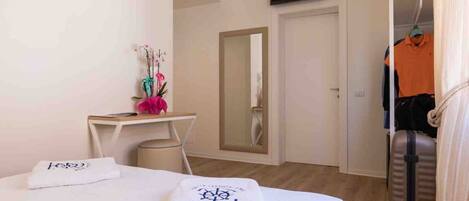 Habitación de hotel con cama, escritorio, espejo, televisor y armario con ropa colgada.