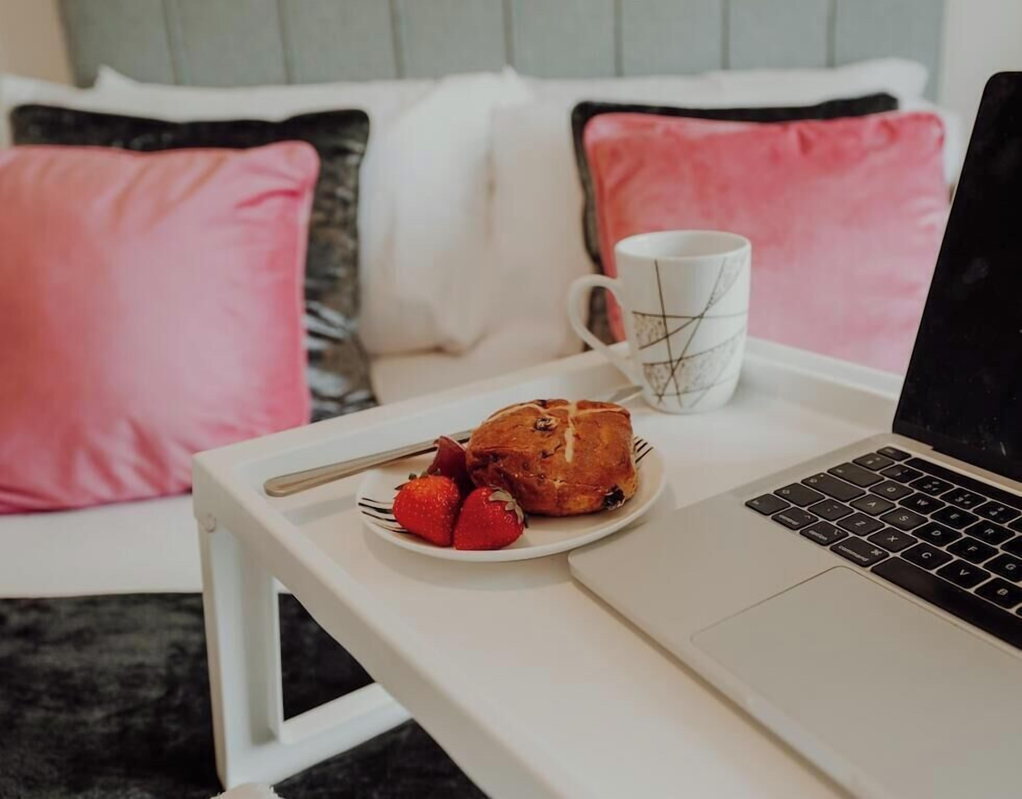 Ein Laptop auf einem weißen Tisch, dazu ein Teller mit Essen und eine Tasse.