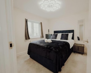 Quarto com uma cama grande, mesa de cabeceira, cortinas na janela e luminária no teto.