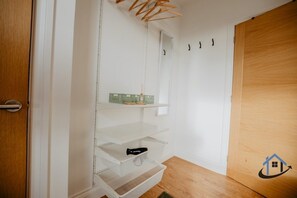 A room with a wooden door, white walls, and a built-in shelving unit with a green basket and a black object.