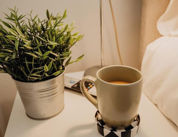 Une plante en pot en métal, une tasse blanche avec un sous-tasse et un téléphone intelligent posés sur une table de chevet.