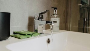 Une salle de bain avec un lavabo blanc, un robinet, un distributeur de savon et un emballage vert posé sur le comptoir.