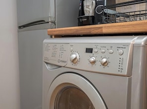 Lavadora de carga frontal con panel de control, encimera de madera y cafetera.