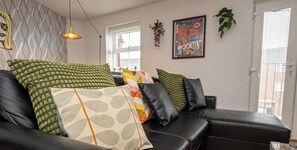 Una sala de estar moderna con un sofá de cuero negro, cojines estampados, una lámpara colgante y una obra de arte enmarcada en la pared.
