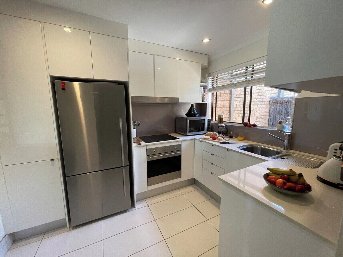 A modern kitchen with stainless steel appliances, white cabinetry, and a window providing natural light.