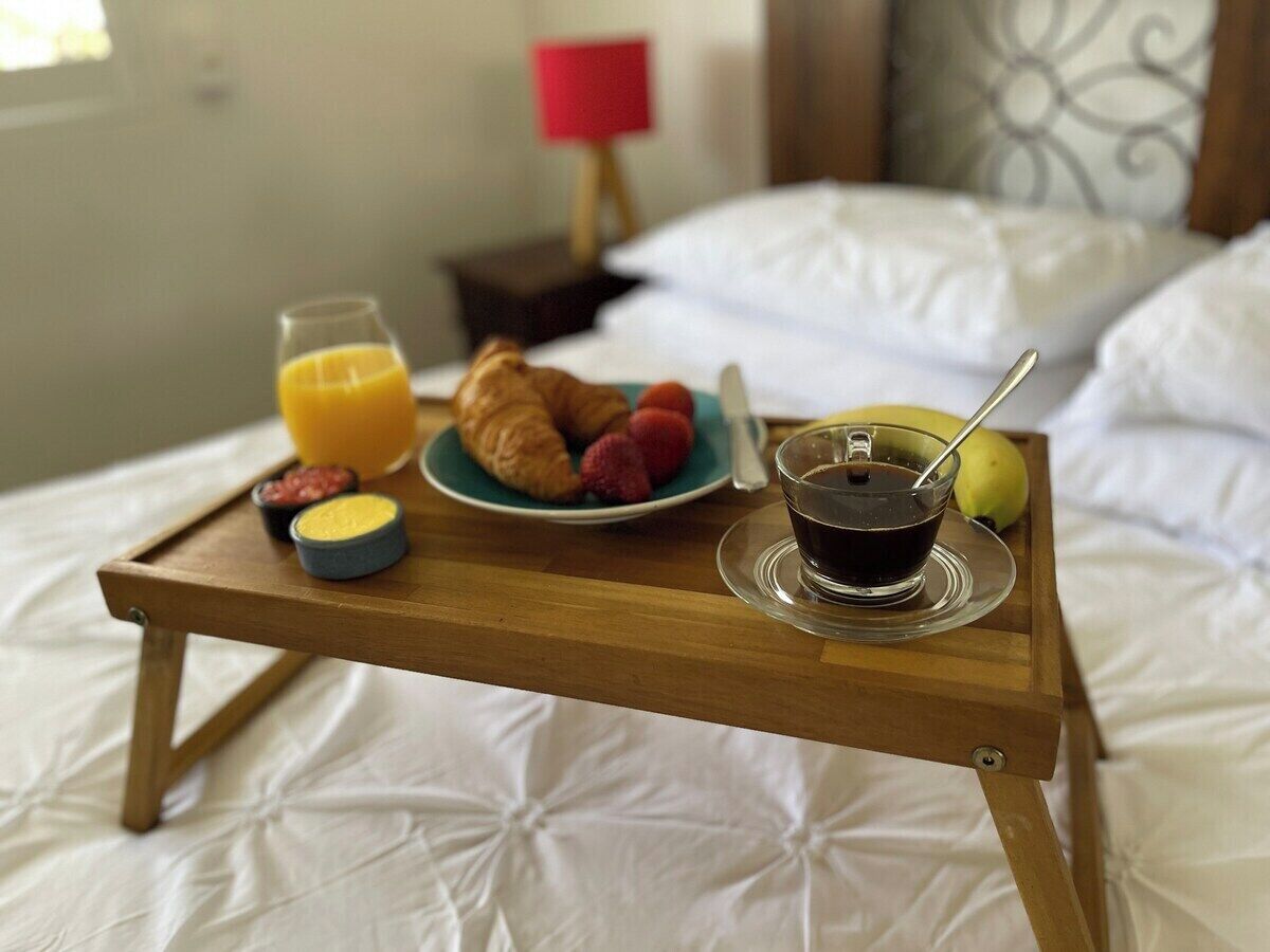 A breakfast tray on a bed with croissants, strawberries, a glass of orange juice, a cup of coffee, and a banana.