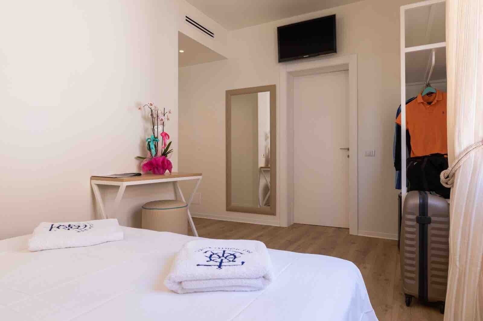 Een hotelkamer met een bed, een bureau, een spiegel, een televisie en een kledingkast met daarin hangende kleding.