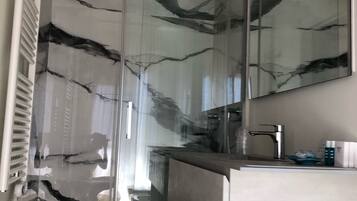 Een moderne badkamer met een glazen douchecabine, een witte wastafel en een grote spiegel.
