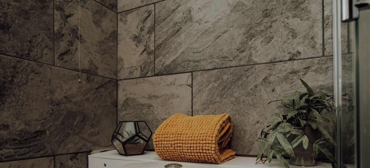 Un baño con pared de mármol, una toalla doblada, un adorno geométrico y una planta en maceta.