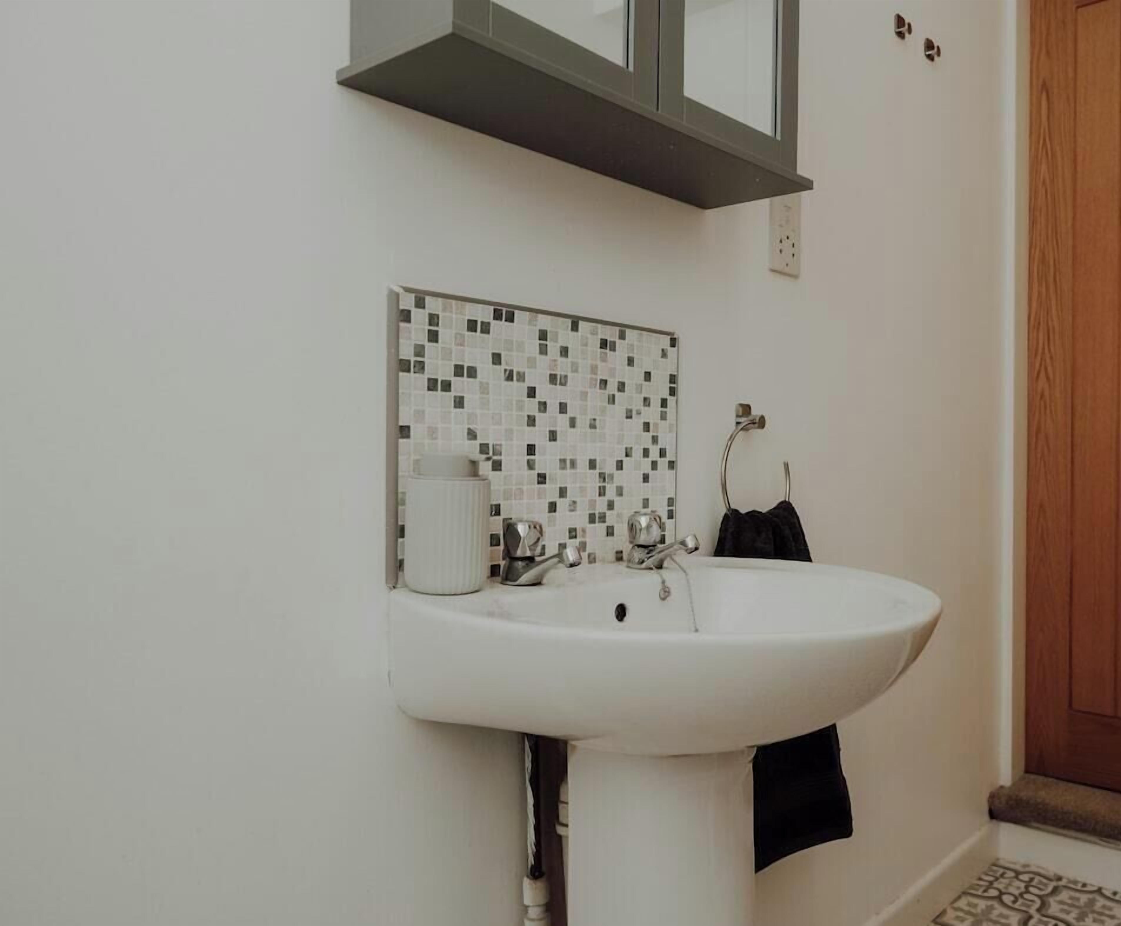 Ein Badezimmer mit einem weißen Waschbecken, einer gefliesten Rückwand, einem Spiegel und einem Handtuchhalter.