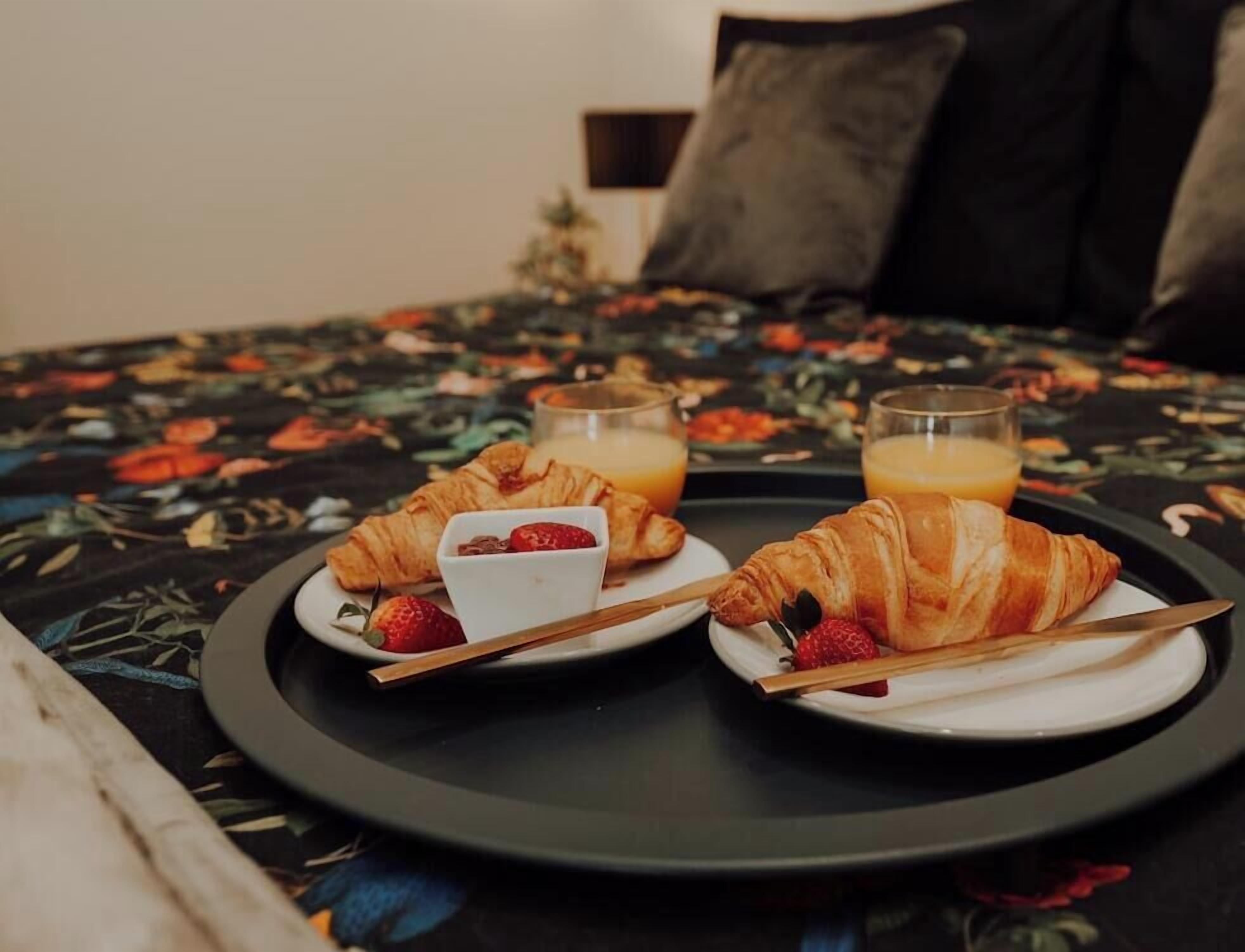 A breakfast setup with croissants and orange juice on a tray, placed on a bed with a floral bedspread.