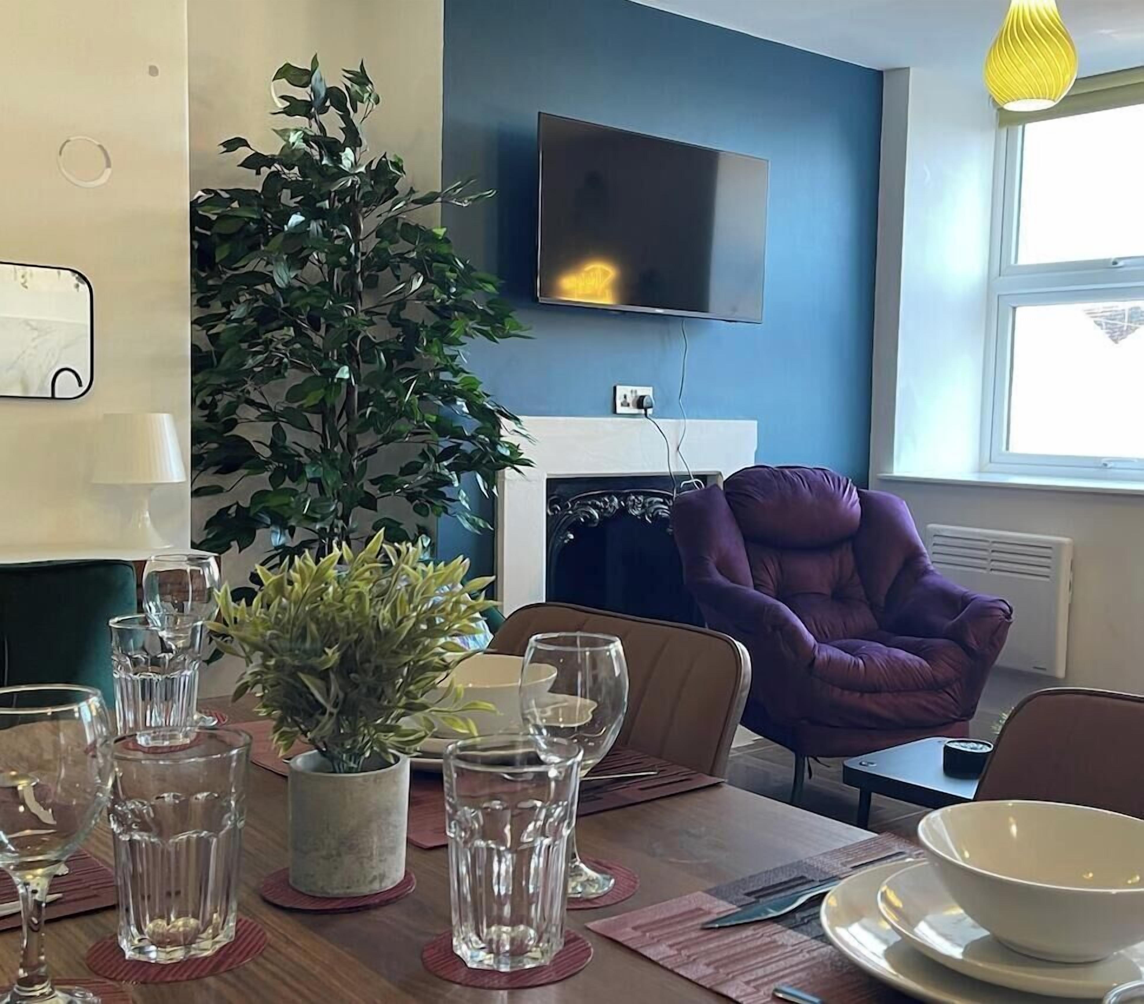 Ein Essbereich mit einem Tisch für zwei Personen, einem Blumentopf und einem an der Wand befestigten Flachbildfernseher.