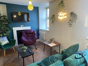A modern living room with a fireplace, a television mounted on the wall, and a comfortable seating area with a sofa and armchairs. - Apt 2 Manor House - 2 Bed 1 bath sleeps 5 parking (Desborough)