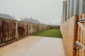 A backyard with a wooden fence, a paved patio, and a grassy lawn. - Dale House, sleeps 7, central, parking x2, garden (Rothwell)