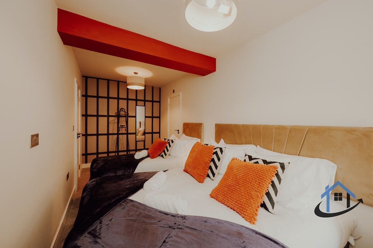 A bedroom with a bed, a red accent wall, a ceiling light, and a window with blinds.