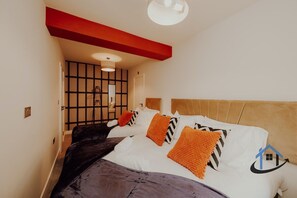 Een slaapkamer met een bed, een rode accentmuur, een plafondlamp en een raam met jaloezieën.
