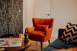 Een kamer met een rode fluweel fauteuil, een gezelschapsspel op een houten tafel, en een behang met patroon.