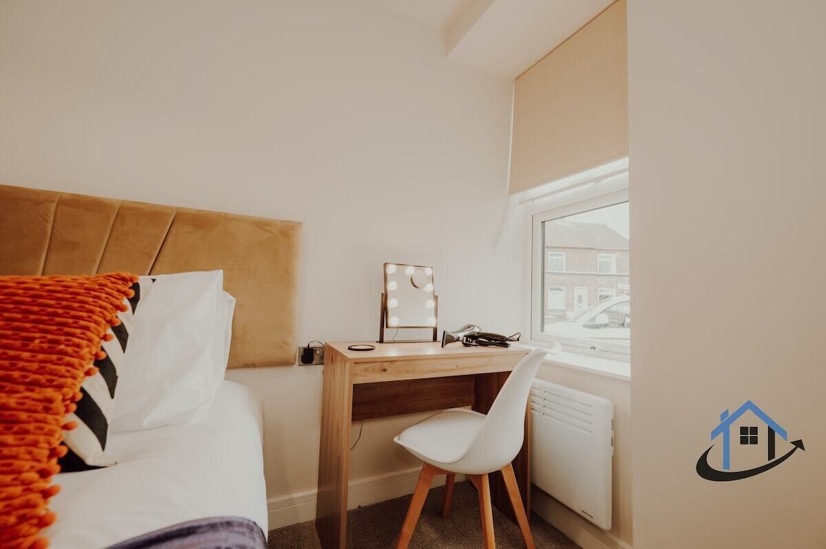 Quarto com cama, escrivaninha com cadeira, janela com persianas e radiador.