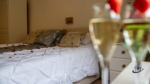 A bedroom with a bed, pillows, a dresser, and a glass of white wine with a strawberry garnish.