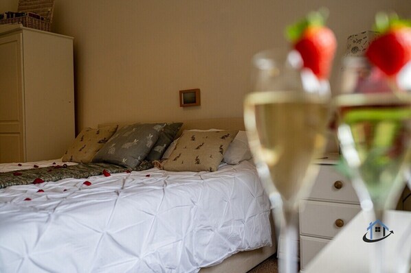 A bedroom with a bed, pillows, a dresser, and a glass of white wine with a strawberry garnish.