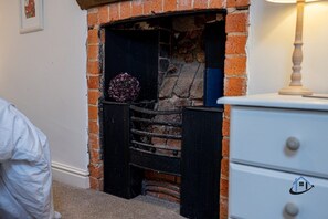 A stone fireplace with a black frame, a decorative item on the mantel, and a white dresser with a logo.
