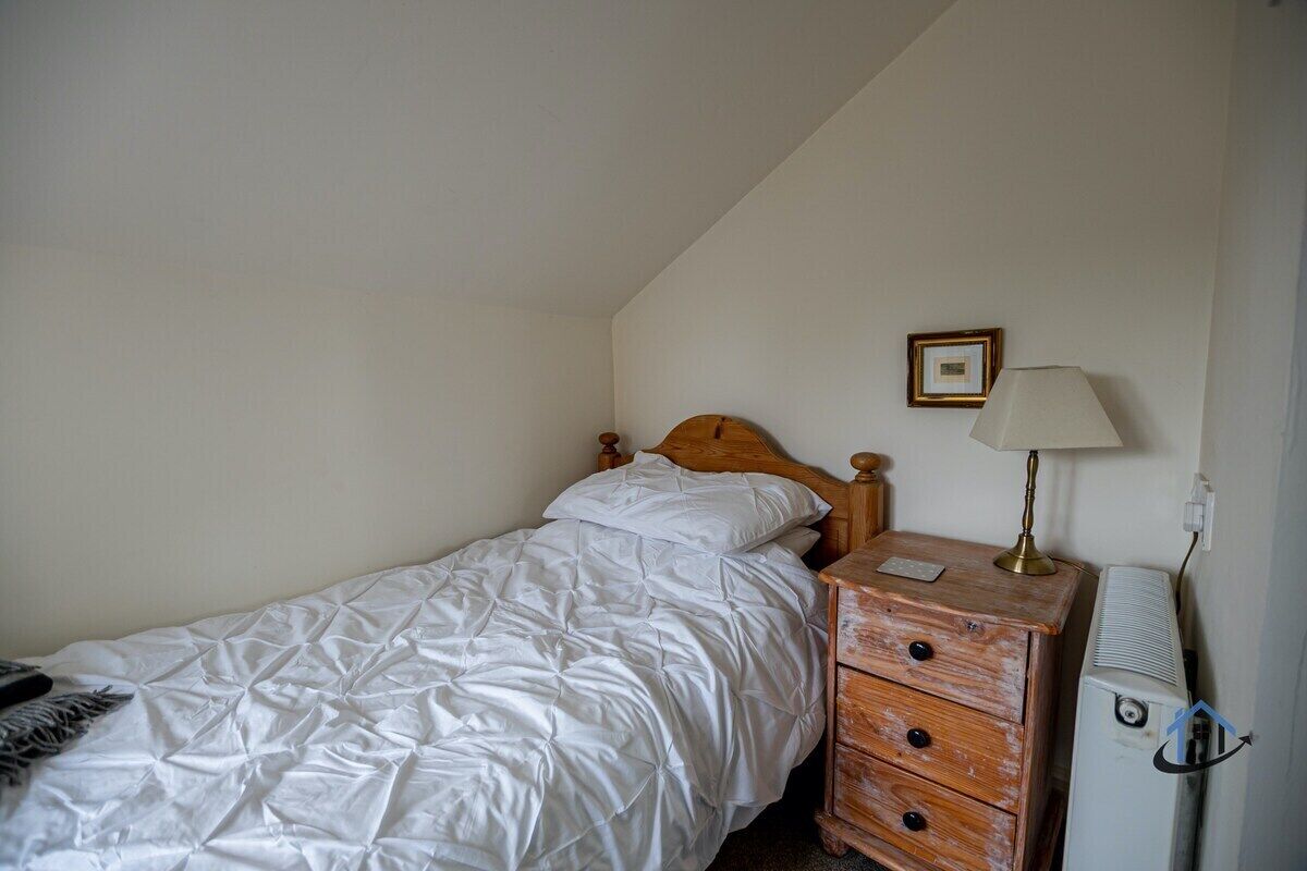 A single bed with a wooden headboard, a bedside table with a lamp, and a small picture frame on the wall.