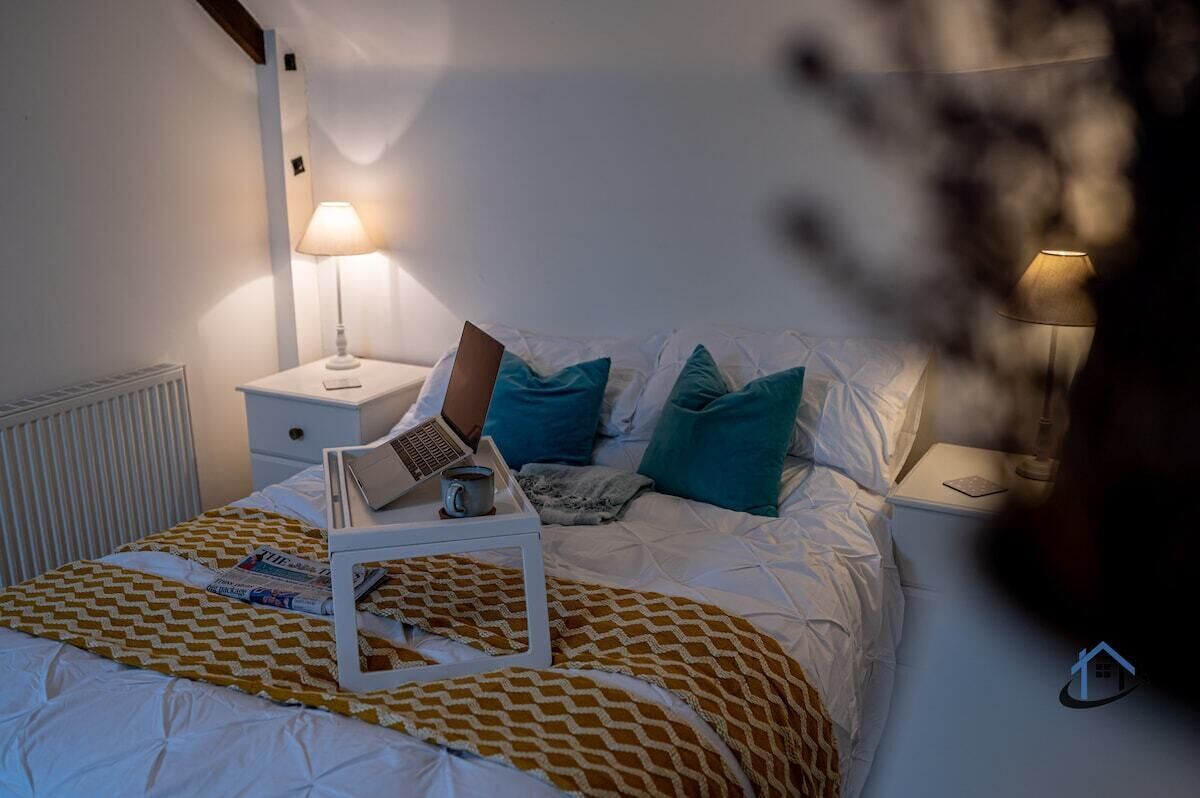 A bedroom with a bed, a nightstand, a lamp, and a tray with a book and a cup.