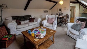 A cozy loft-style living room with a high ceiling, exposed beams, and a dining area with a wooden table and chairs.
