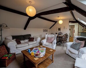 A cozy loft-style living room with a high ceiling, exposed beams, and a dining area with a wooden table and chairs.