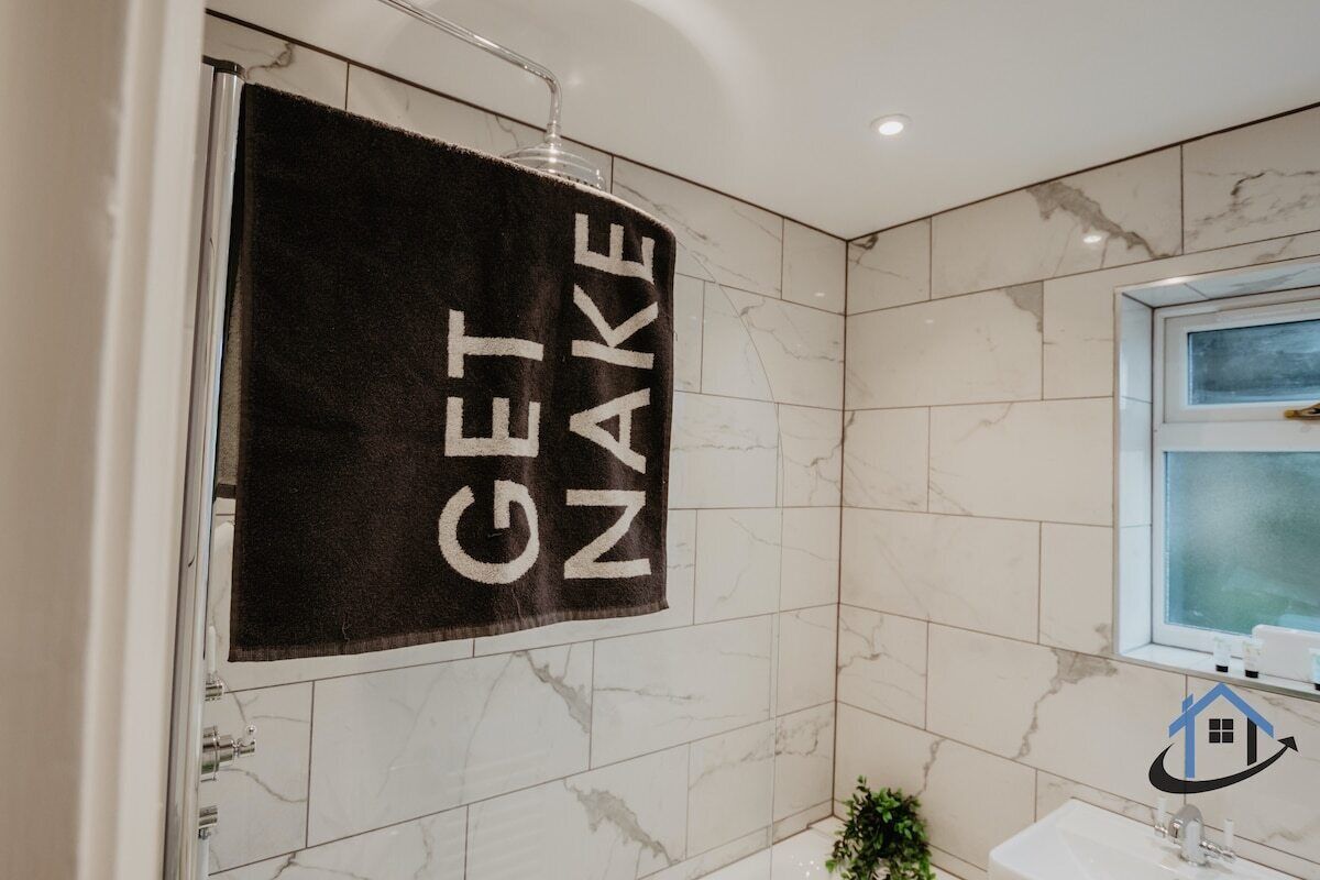 A bathroom with a towel hanging on the wall that reads 'GET NAKE.'